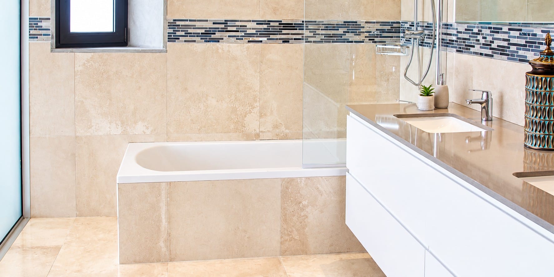 Bathroom with fitted bathtub, glass shower screen, mosaic tile border and white vanity unit