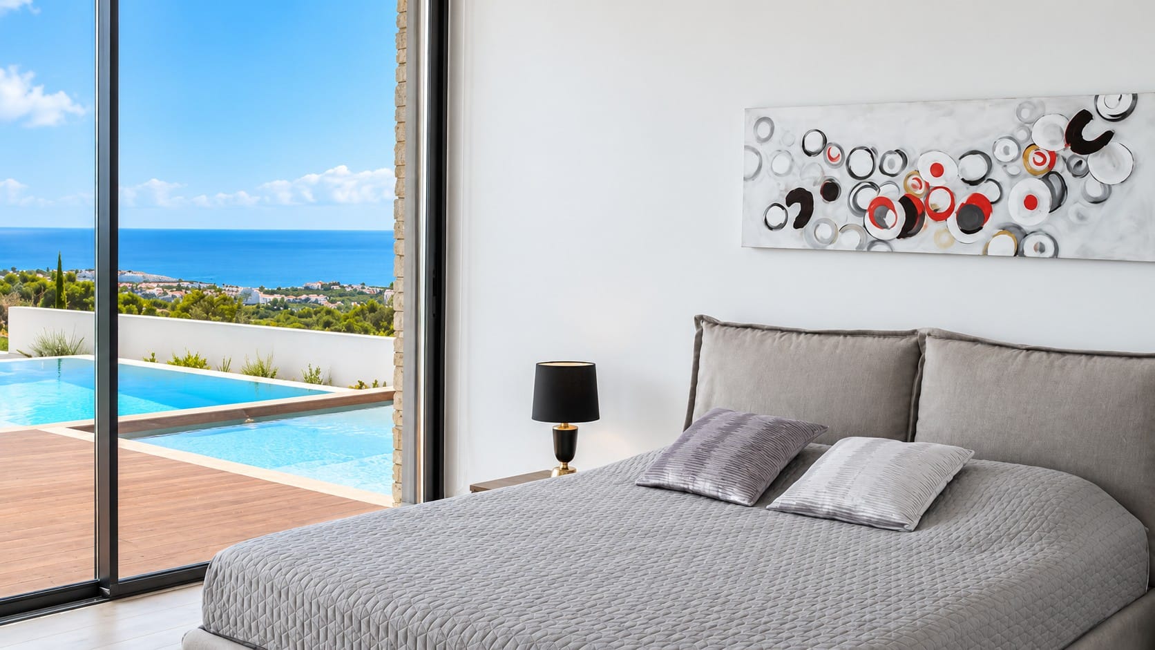 Bedroom with full-height sliding glass doors opening onto a pool deck with views towards the Mediterranean Sea