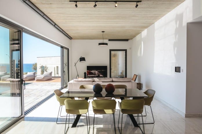 Furnished dining area with glass table and chairs, living area beyond and sliding glass doors opening onto a terrace with sea views