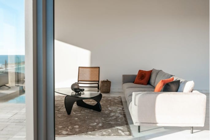 Furnished living area with sofa, coffee table and armchair beside full-height glazing with a view of the sea
