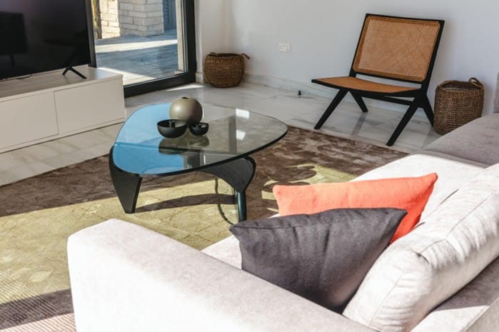 Living area with sofa, glass coffee table, armchair and TV unit beside glazed doors to the terrace