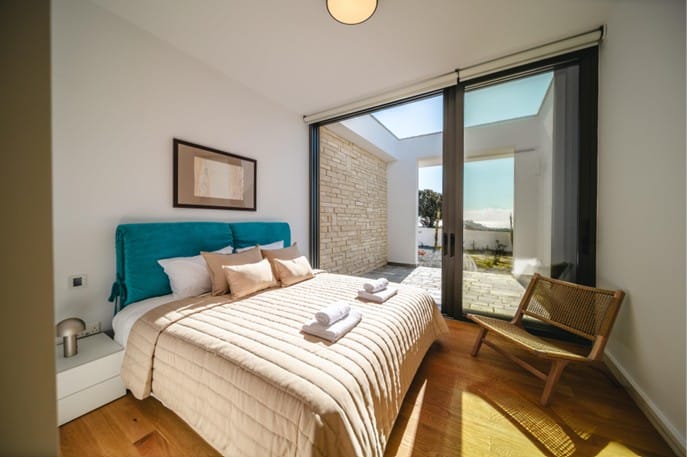 Furnished bedroom with double bed, oak parquet flooring and sliding glass doors opening onto a paved courtyard