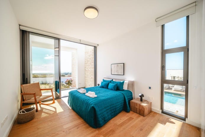 Furnished bedroom with double bed, oak parquet flooring and large windows, including a view of the swimming pool
