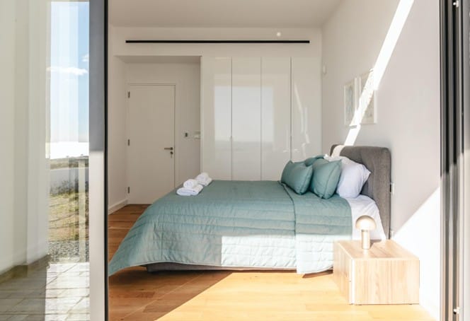 Furnished bedroom with double bed, fitted wardrobes and oak parquet flooring, seen through a glass door