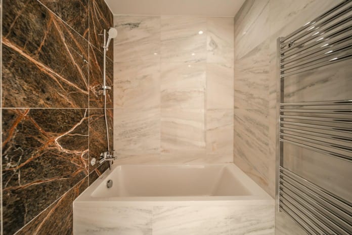 Bathtub with hand shower, marble-effect wall tiles and chrome heated towel rail
